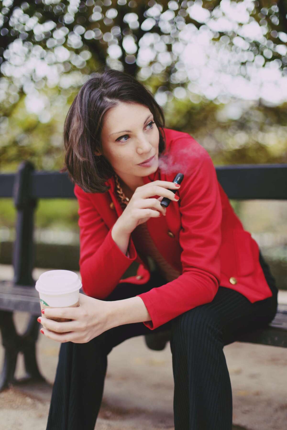 woman vaping on a bench drinking coffee